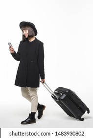 Full Length Side Portrait Of Smiling Asian Woman Walking Against Isolated White Background With Suitcase And Cellphone