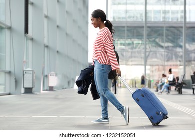 Full Length Side Portrait Of Young Black Woman Walking With Suitcase In Airport