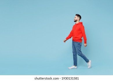 Full Length Side Profile View Of Young Caucasian Smiling Bearded Handsome Student Man 20s In Casual Red Orange Hoodie Walking Going Isolated On Blue Background Studio Portrait People Lifestyle Concept