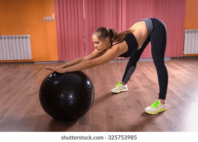 Full Length Side Profile of Young Woman Wearing Exercise Clothing Stretching with Help of Inflatable Exercise Ball in Colorful Dance Studio