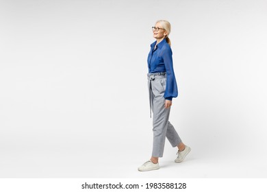 Full length side view blonde pensive happy successful employee business woman 40s in blue classic shirt gray pants glasses formal clothes walking going isolated on white background studio portrait