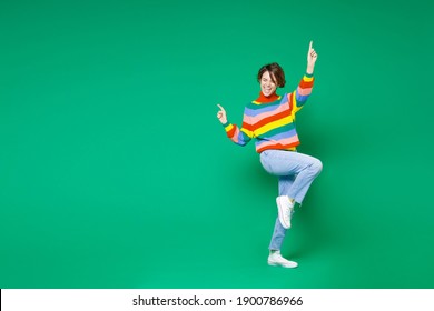 Full length side view of cheerful funny young brunette woman 20s in casual colorful sweater dancing pointing index fingers up winner gesture isolated on bright green color background studio portrait Arkivfotografi