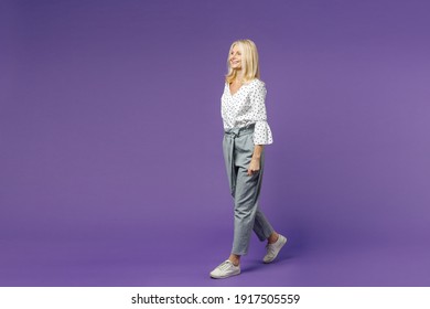 Full Length Side View Of Cheerful Beautiful Elderly Gray-haired Blonde Woman Lady 40s 50s In White Dotted Blouse Walking Going Looking Aside Isolated On Bright Violet Color Background Studio Portrait