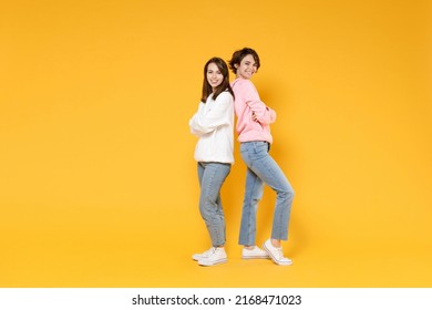 Full Length Side View Of Cheerful Two Young Women Friends 20s Wearing Casual White Pink Hoodies Standing Back To Back Holding Hands Crossed Isolated On Bright Yellow Color Background Studio Portrait