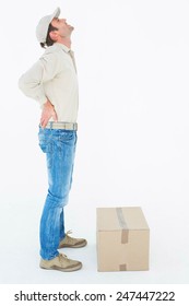 Full length side view of delivery man suffering from back pain standing by cardboard box against white background