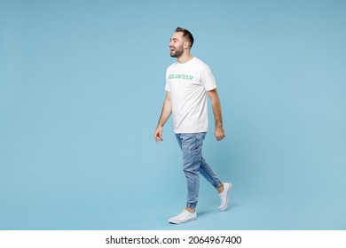 Full Length Side View Excited Young Man In White Volunteer T-shirt Looking Aside Walking Going Isolated On Blue Background Studio Portrait. Voluntary Free Work Assistance Help Charity Grace Concept