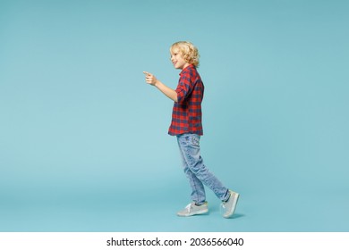 Full Length Side View Of Funny Little Curly Kid Boy 10s In Basic Red Checkered Shirt Pointing Index Finger Aside Isolated On Blue Wall Background Children Studio Portrait. Childhood Lifestyle Concept