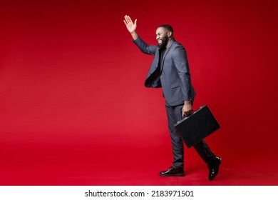 Full length side view of funny young african american business man 20s in classic jacket suit hold briefcase waving greeting with hand looking aside isolated on bright red background studio portrait - Powered by Shutterstock