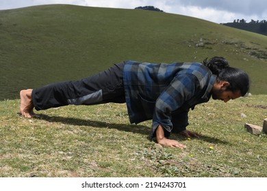 Full length side view of a handsome long haired Indian young man doing push ups in the mountain