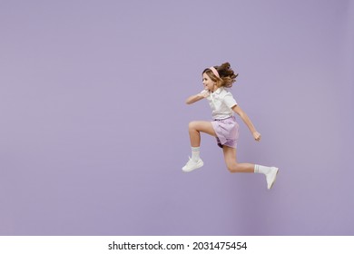 Full length side view of little fun overjoyed kid girl 12-13 years old in white short sleeve shirt jumping high run fast hurrying up isolated on purple background Childhood children lifestyle concept.