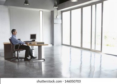 Full Length Side View Of A Man Sitting At Desk In Empty Office