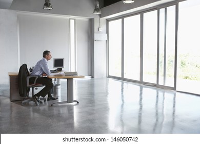 Full Length Side View Of A Man Sitting At Desk In Empty Office