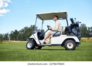 Full length side view of man driving golf cart across green field in sports club, copy space - Powered by Shutterstock