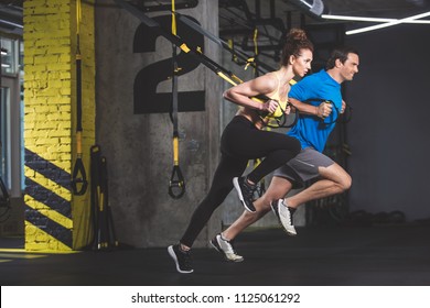 Full length side view outgoing male and concentrated girl doing exercise with functional loops. They situating in gym - Powered by Shutterstock