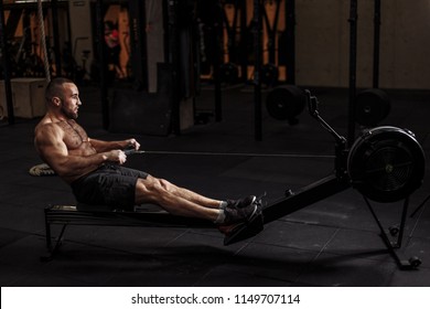 Full Length Side View Photo.young Fit Guy Is Concentrated On The Exercise With Indoor Rower At Gym