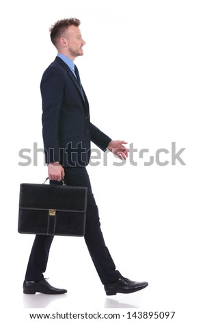 full length side view picture of a young business man walking with a suitcase in his hand and a smile on his face. on white background