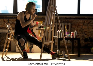 Full length side view portrait of handsome male artist painting on easel while enjoying work in art studio lit by sunlight, copy space