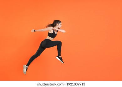 Full Length Side View Of Portrait Of Young Fitness Sporty Woman 20s Wearing Black Sportswear Posing Training Working Out Jumping Like Running Looking Aside Isolated On Orange Color Background Studio