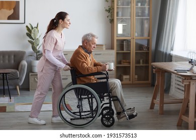 Full length side view portrait of senior man in wheelchair with nurse assisting him at retirement home, copy space