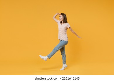 Full Length Side View Portrait Of Shocked Amazed Young Woman Wearing Pastel Pink Casual T-shirt Posing Holding Hand At Forehead Looking Far Away Distance Isolated On Yellow Color Background Studio