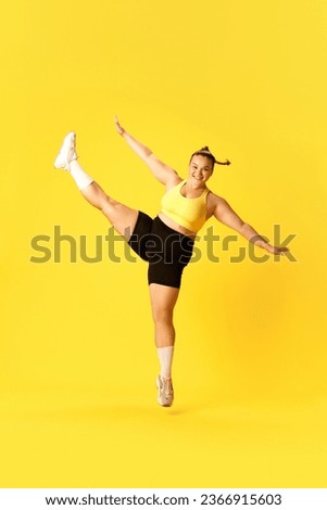 Full length side view portrait of plus size woman dressed sporty training, jumping with one leg up against over yellow background. Concept of sport, hobby, health, lifestyle, healthy eating, workout.