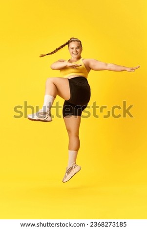 Full length side view portrait of plus size woman dressed sporty training long, high jumps against over yellow background. Concept of sport, hobby, health, lifestyle, healthy eating, workout. ad
