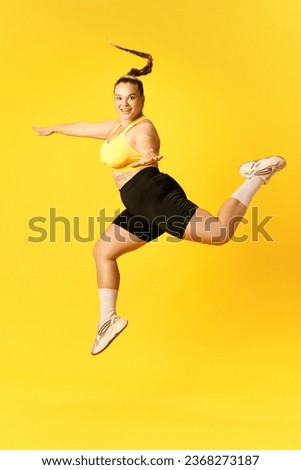 Full length side view portrait of plus size sports woman in tracksuit training long, high jumps against over yellow background. Concept of sport, hobby, health, lifestyle, healthy eating, workout. ad