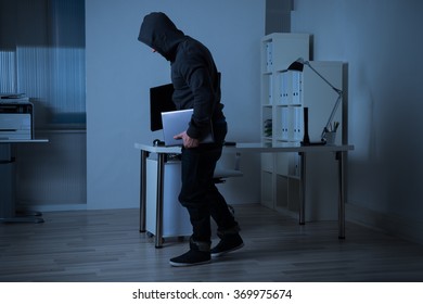 Full Length Side View Of Robber Stealing Laptop From Office At Night