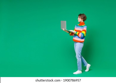 Full length side view of smiling funny young brunette woman 20s years old wearing basic casual colorful sweater working on laptop pc computer isolated on bright green color background studio portrait - Shutterstock ID 1900786957