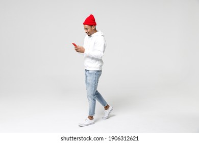 Full Length Side View Of Smiling Young African American Man 20s Years Old In Casual Streetwear Hoodie Using Mobile Cell Phone Typing Sms Message Isolated On White Colour Background, Studio Portrait