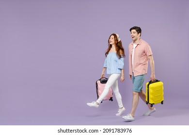 Full length side view two traveler tourist woman man couple in shirt holding suitcase walking go isolated on purple background. Passenger travel abroad on weekends getaway. Air flight journey concept