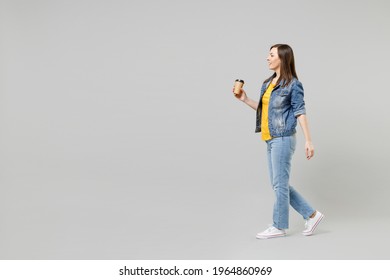 Full length side view walk young happy caucasian woman in casual denim jacket yellow t-shirt holding in hand paper cup of coffee drink tea isolated on grey background studio. People lifestyle concept - Powered by Shutterstock