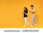 Full length side view young couple of African American ethnicity two friend family man woman wear black t-shirt show hold use mobile cell phone walk isolated on yellow color background studio portrait