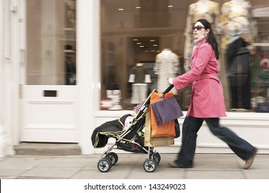 Full Length Side View Of Young Mother Pushing Baby Stroller By Clothes Shop