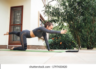 Full length side view of young woman learning balancing table pose on laptop in backyard. High quality photo