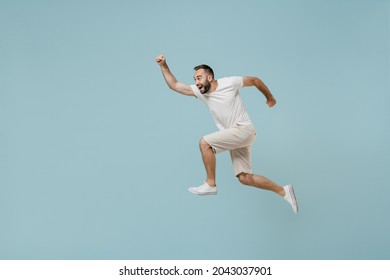 Full Length Side View Young Excited Happy Sportsman Runner Man 20s Wearing Casual White T-shirt Jump High Run Fast Hurrying Up Isolated On Plain Pastel Light Blue Color Background Studio Portrait.