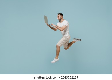 Full Length Side View Young Overjoyed Man 20s In Casual White T-shirt Jump High Run Fast Hurrying Up Hold Closed Laptop Pc Computer Isolated On Plain Pastel Light Blue Color Background Studio Portrait