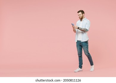 Full length side view young smiling unshaven man 20s in blue striped shirt hold mobile cell phone chat online browsing internet walk isolated on pastel pink background studio. Tattoo translate fun. - Shutterstock ID 2050811126