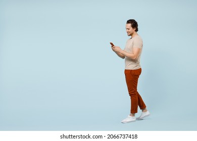 Full length side view young smiling happy caucasian man wear casual basic beige t-shirt hold mobile cell phone chat online isolated on pastel blue background studio portrait. People lifestyle concept - Shutterstock ID 2066737418