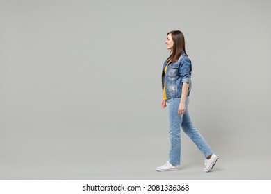 Full length side view young caucasian woman 20s wearing casual denim jacket yellow t-shirt looking aside walking going strolling isolated on grey background studio portrait People lifestyle concept