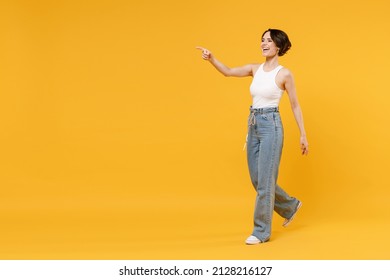 Full length side view young woman 20s with bob haircut wearing white tank top shirt walking go point index finger aside on workspace area mock up isolated on yellow background People lifestyle concept