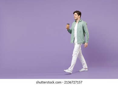 Full length side view young smiling man 20s in casual green mint shirt white t-shirt holding paper cup of coffee drink hot tea in morning walk go isolated on purple color background studio portrait - Powered by Shutterstock