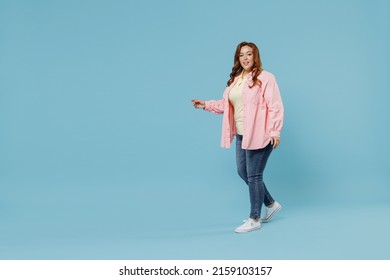 Full Length Side View Young Fun Smiling Redhead Chubby Overweight Woman 30s Wearing In Pink Shirt Jeans Casual Clothes Walking Going Looking Camera Isolated On Pastel Blue Background Studio Portrait.