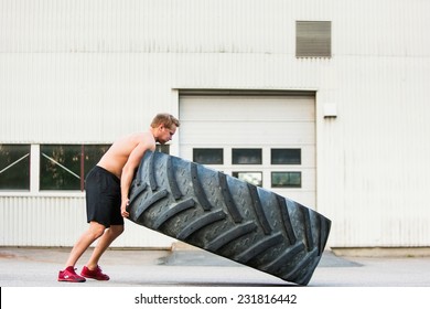 Full length side view of young male athlete flipping large tire outside gym - Powered by Shutterstock