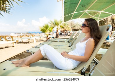 Full Length Side View Of Young Woman Relaxing On Lounge Chair At Beach