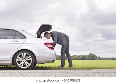 Full length side view of young businessman looking in car trunk at countryside