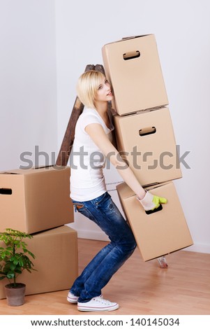 Full length side view of young woman carrying heavy cardboard boxes in house
