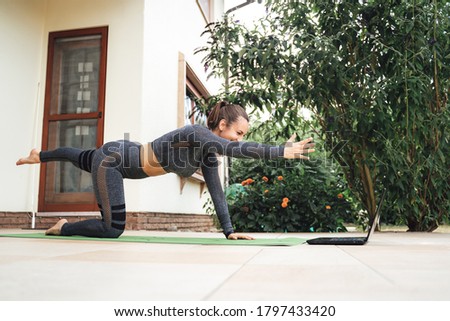Full length side view of young woman learning balancing table pose on laptop in backyard. High quality photo