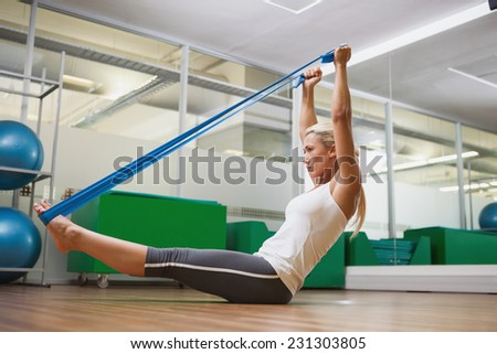 Full length side view of a young woman using resistance band in fitness studio