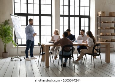 Full length skilled young speaker standing near whiteboard with statistics sales data, presenting corporate marketing strategy to attentive diverse multiracial teammates and company leaders in office. - Powered by Shutterstock